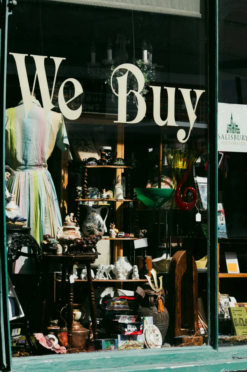 A shop window display filled with vintage collectibles, ceramics, and a striped dress