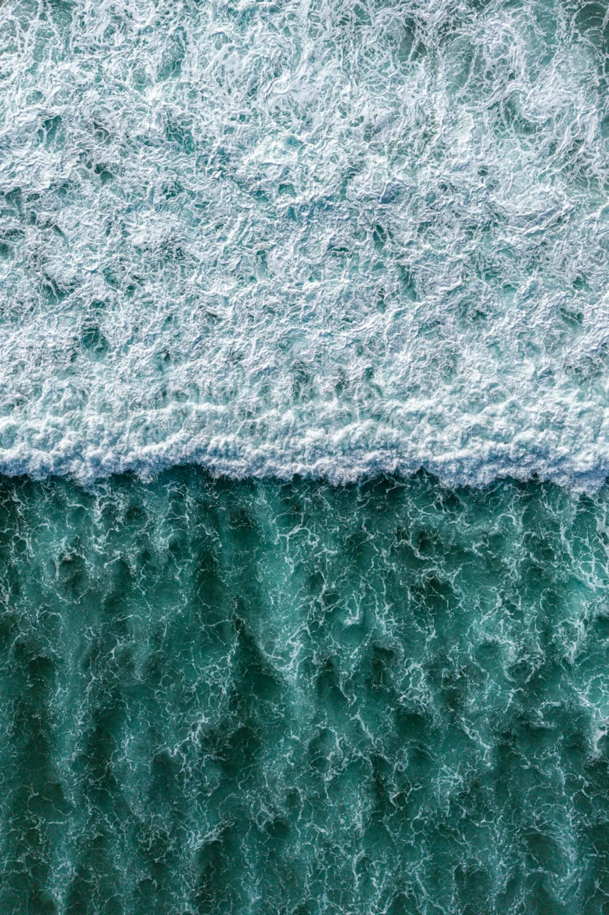 Aerial view of foamy ocean waves meeting turquoise water