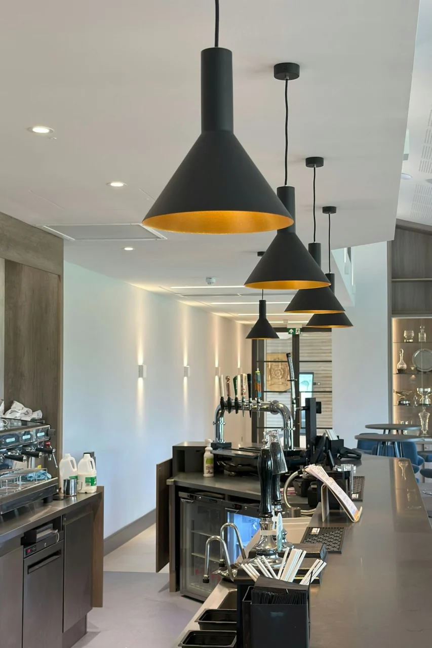 Black pendant lights hanging over a long bar counter in a modern cafe