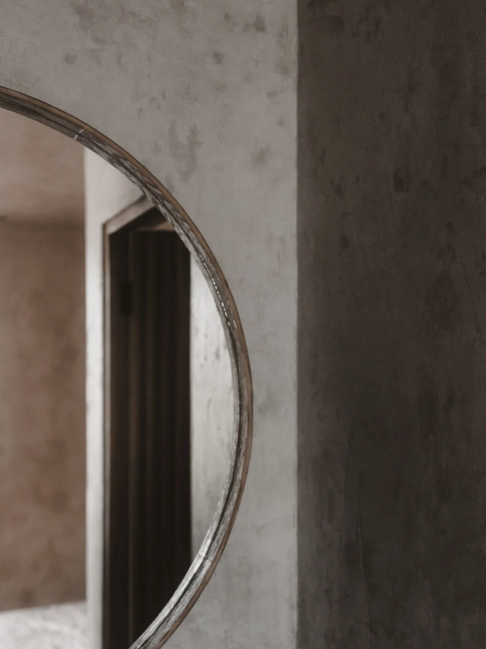 Tall narrow mirror with thin brushed steel frame mounted opposite the entry reflecting the hallway s light greige walls and a glimpse of a distant landscape painting emphasizing depth without clutter